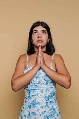 Çiçekli elbiseli kadın bej arka planda el ele dua ediyor..