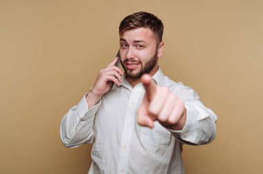 Beyaz gömlekli bir adam telefonla konuşuyor ve kamerayı işaret ediyor..