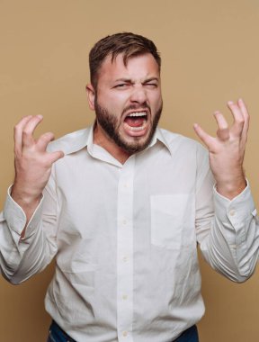 Beyaz gömlekli adam bej arka planda öfke gösteriyor.