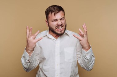 Beyazlar içinde hayal kırıklığına uğramış bir adam bej bir arka plana karşı öfkesini dile getiriyor..