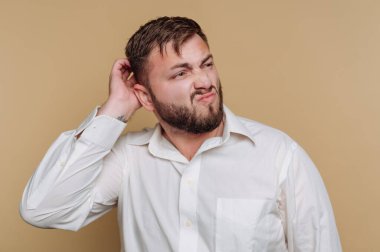 Beyaz gömlekli bir adam kafası karışık bir şekilde kaşınıyor..