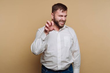 Beyaz gömlekli bir adam bej arka planda şakacı bir pençe hareketi yapıyor..