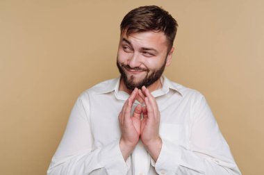 Beyaz gömlekli, bej arka planda yaramaz bir yüz ifadesi olan bir adam..