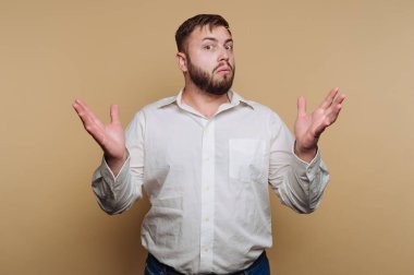 Beyaz gömlekli, bej arkaplanlı, kafası karışmış bir adam.