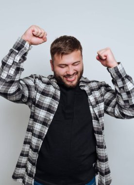 Ekose gömlek ve siyah tişört giymiş, arka planda sevinçle gülümseyen genç bir adam.