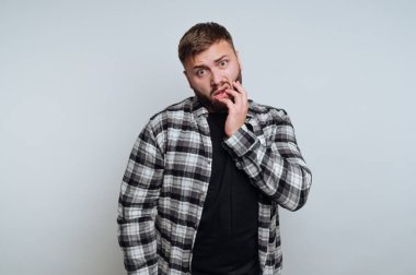 Ekose gömlekli adam gri arka planda kafası karışmış görünüyor.