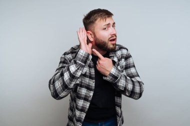 Ekose gömlekli bir adam, kulak kabartıyor, jest yapıyor..