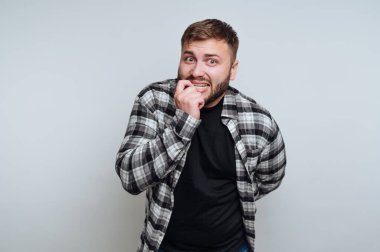 Ekose gömlekli bir adam tırnaklarını yiyor, endişeli görünüyor..