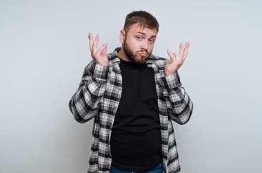 Kareli gömlekli genç adam, kafası karışmış bir ifadeyle omuz silkiyor..