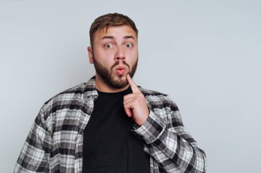 Yüzü şaşkın, ekose gömlekli, dudakları parmaklı bir adam..