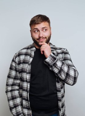 Gri bir arka plana karşı düşünceli bir ifadeyle ekose gömlekli bir adam..