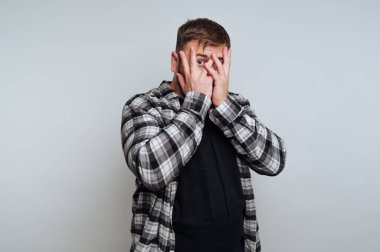 Ekose gömlekli bir adam parmaklarının arasından gizlice bakıyor..