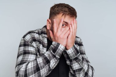 Ekose gömlekli adam elleriyle yüzünü kapatıyor, parmaklarının arasından dikizliyor..