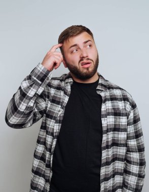 Ekoseli tişörtlü bir adam parmağıyla şakağı düşünüyor.