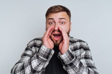 Ekose gömlekli bir adam elleri ağızda bağırıyor..