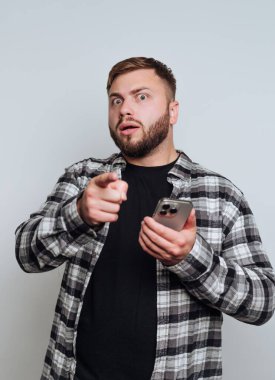 Ekose gömlekli bir adam, şaşırmış bir ifadeyle, elinde telefonla..