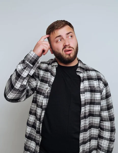 Ekoseli tişörtlü bir adam parmağıyla şakağı düşünüyor.