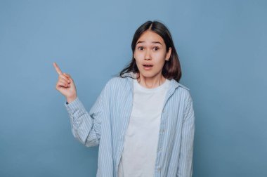 Şaşırmış bir kadın mavi bir arka plana işaret ediyor..