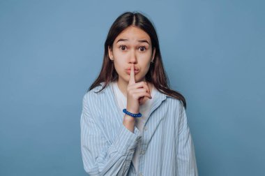 Genç bir kadın mavi bir arka plana karşı sessiz bir jest yapıyor..