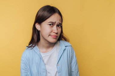 Sarı arka planda şüpheli bir ifadeye sahip genç bir kadın..