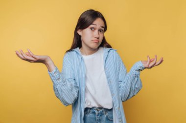 Sarı arka planda, kafası karışık bir ifadeyle omuz silken genç bir kadın..