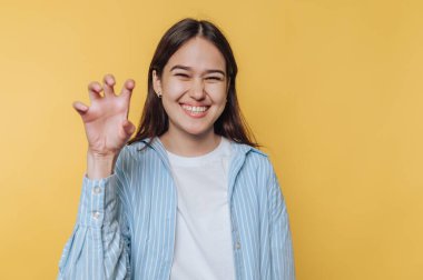 Gülümseyen kadın şakacı bir şekilde sarı arka plana pençe hareketi yapıyor..
