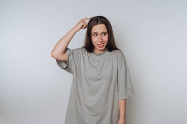Gri tişörtlü, kafasını kaşıyan, kafası karışmış bir kadın..