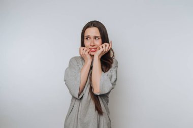 Gri gömlekli kadın beyaz arka planda endişeli görünüyor.