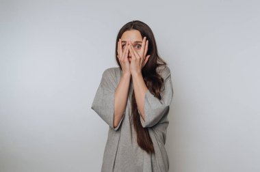 Gri gömlekli, uzun saçlı kadın şaşırmış görünüyor, elleri yüzlerinde..