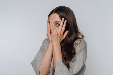 Şaşırmış bir ifadeyle parmaklarının arasından bakan bir kadın..