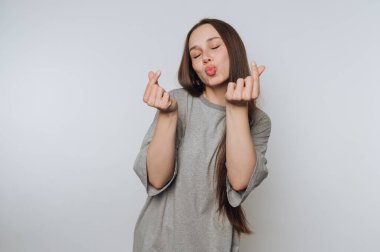 Genç bir kadın kalp hareketi yapıyor. Gri bir gömlek giyiyor..