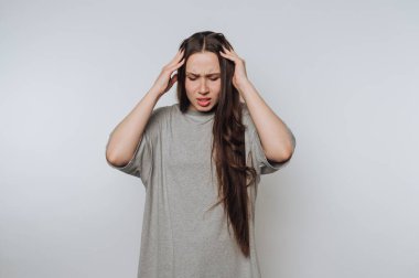 Gri gömlekli kadın başını tutuyor, stresli ya da acı içinde görünüyor..