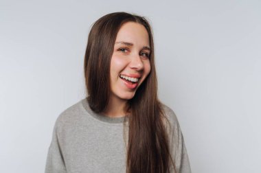 Gri kazaklı, uzun kahverengi saçlı, gülümseyen genç kadın.