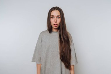 Gri gömlekli, uzun saçlı kadın şaşırmış görünüyor.