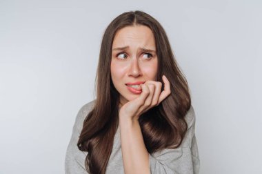 Uzun kahverengi saçlı, endişeli ve endişeli görünen, tırnaklarını yiyen genç bir kadın.