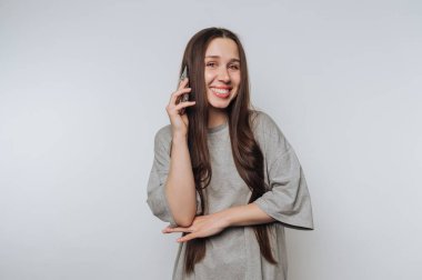 Gülümseyen kadın gri arka planda akıllı telefondan konuşuyor.