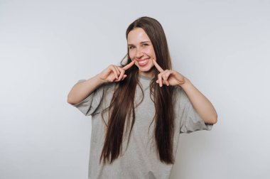 Smiling woman with long hair pointing at her cheeks.