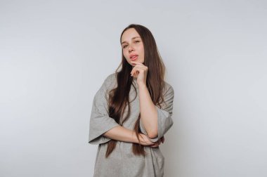 Gri gömlekli genç bir kadın düşünceli bir ifadeyle poz veriyor..