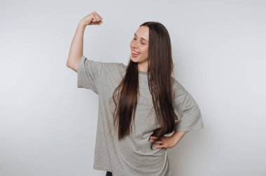 Gri gömlekli genç bir kadın kol kaslarını esnetiyor, gülümsüyor..