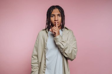 Parmakları dudaklarında genç adam, sessiz, pembe arka plan sinyali veriyor..