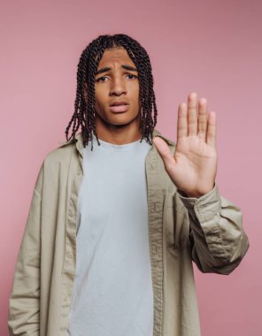 Örgülü genç adam pembe arka plana karşı jest yapıyor..