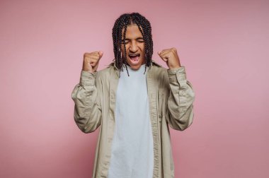 Örgülü saçlı, pembe arka planda yumruklarıyla kutlama yapan biri..