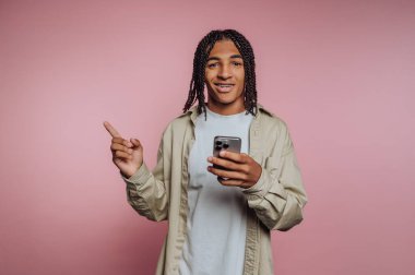 Saçları örgülü, akıllı bir telefon tutan, gülümseyen genç bir adam..