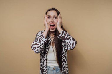 Uzun saçlı ve bej arka planda desenli gömlekli, şaşırmış bir kadın..