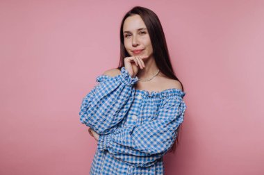 Mavi elbiseli kadın pembe arka planda poz veriyor.