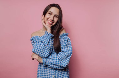 Pembe arka planda mavi kareli elbiseli gülümseyen kadın.