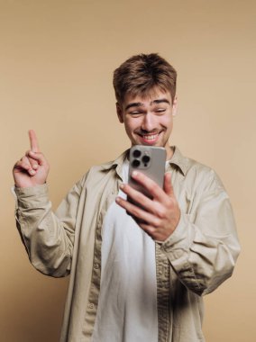 Genç adam gülümsüyor ve akıllı telefona bakarken işaret ediyor.