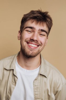 Bej arka planda sakallı, gülümseyen genç bir adam..