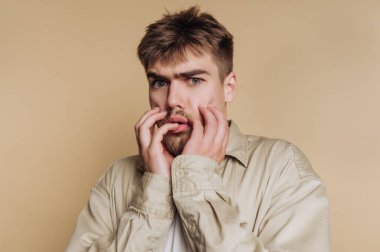 Bej arkaplanda endişeli bir ifadesi olan genç adam..