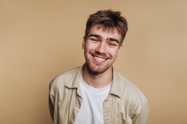 Bej arka planda sakallı, gülümseyen genç bir adam..